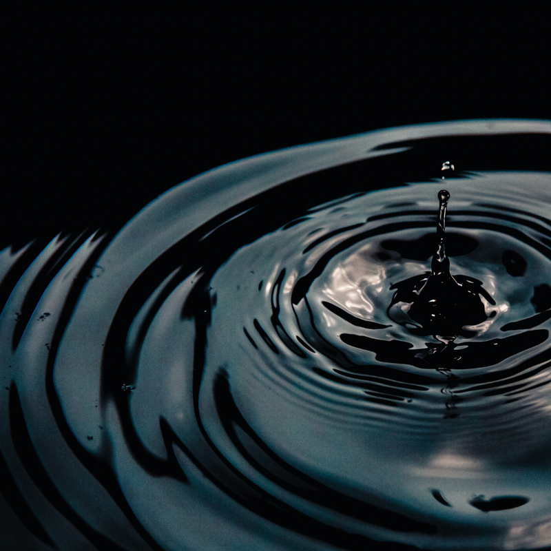 Close-up of a water droplet creating ripples on water with a black background