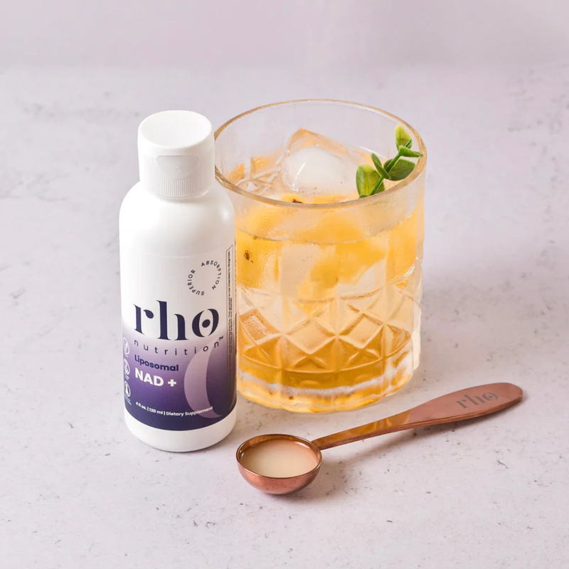Bottle of rho nutrition supplement next to a glass of iced drink with a spoon on a light surface